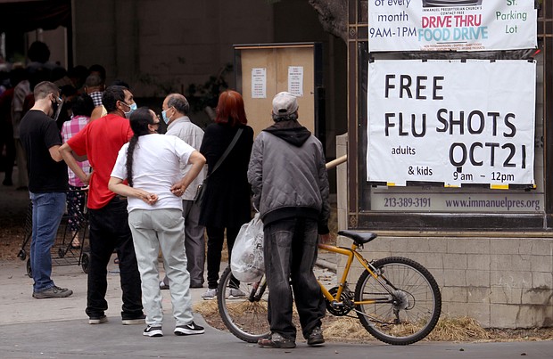 People look over a sign advertising a free flu shot clinic provided by Cedars-Sinai Hospital and Good Samaritan Hospital in the parking lot of Immanuel Presbyterian Church in Los Angeles on October 21, 2020.
Credit:	Genaro Molina/Los Angeles Times/Getty Images