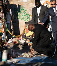 Philonise Floyd, center, the brother of the late George Floyd, puts his hand on the spot where Mr. Floyd died at 39th Street and Chicago Avenue in Minneapolis last May at the hands of police. Members of the Floyd family visited the memorial site on March 12, shortly after a news conference announcing a $27 million settlement in their civil case against the City of Minneapolis. The family also met with several businesses in the area to express their support.