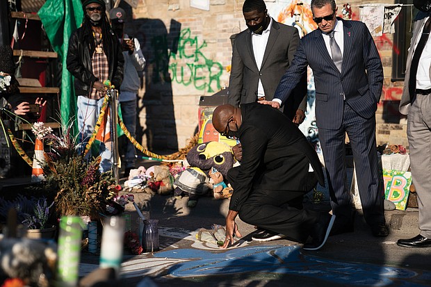 Philonise Floyd, center, the brother of the late George Floyd, puts his hand on the spot where Mr. Floyd died at 39th Street and Chicago Avenue in Minneapolis last May at the hands of police. Members of the Floyd family visited the memorial site on March 12, shortly after a news conference announcing a $27 million settlement in their civil case against the City of Minneapolis. The family also met with several businesses in the area to express their support.