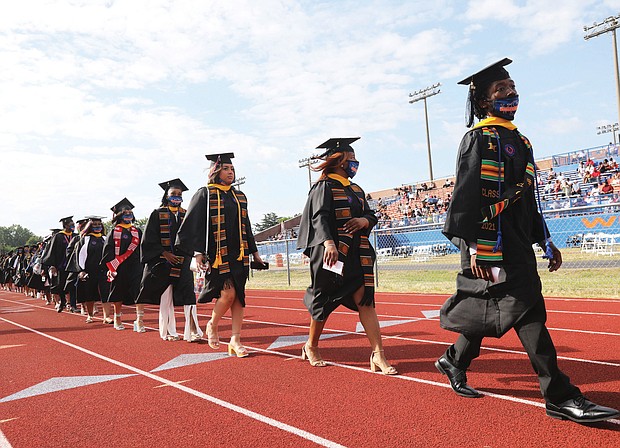 Jamal Meekins, 22, right, a psychology major from Surry County, walks with fellow graduates during the procession Sunday at Virginia State University’s commencement in Rogers Stadium for the classes of 2020 and 2021. Mr. Meekins, who earned his degree this spring, will begin nursing school next week.