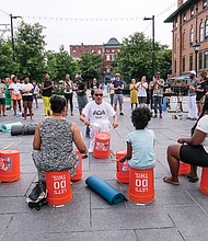 People participate in a community drum circle led by Ram Bhagat of Drums No Guns at Saturday’s Juneteenth Freedom Day at the 17th Street Market in Shockoe Bottom.