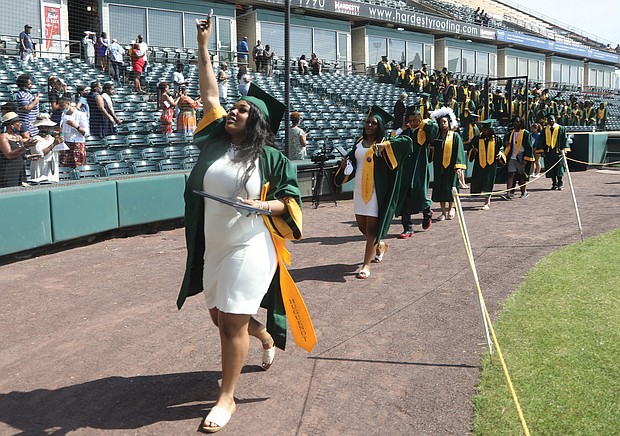 Kym Idella Jeter waves to family and friends in the stands as she walks out with Huguenot High School’s new graduates at the end of Monday morning’s ceremony at The Diamond on Arthur Ashe Boulevard. Huguenot’s was the first of eight Richmond high school commencements over three days at the ballpark.