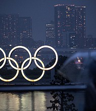 A woman walks past the Olympic Rings lit up at dusk in the rain, on the Odaiba waterfront in Tokyo on July 9. An unnamed US female gymnast has tested positive for Covid-19, Inzai city official Takamitsu Ooura told CNN.
Mandatory Credit:	CHARLY TRIBALLEAU/AFP/Getty Images