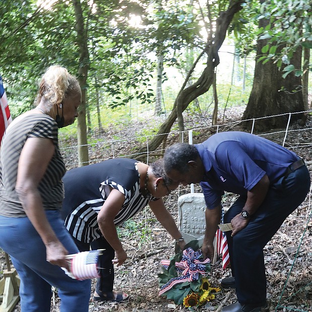 Honoring a Buffalo Soldier/Descendants of Moses Bradford Jr. of Henrico County, a Buffalo Soldier who served in the 25th Infantry during the Spanish-American War, place a wreath on his grave during a twilight memorial service at the Sons and Daughters of Ham Cemetery near Bandy Field in Henrico County on July 28. The family members, from left, Diane Winston Jones, Linda Truman Nash and Spencer Truman, participated in the local commemoration on National Buffalo Soldiers Day, which honors the contributions of some of the earliest African-American troops in the U.S. military. The commemoration included a three-volley salute by members of the Veterans of Foreign Wars Post 9808 in Mechanicsville, and a flag presentation, below, by Najiek Harris, 15, left, and Christian Hicks, 13, of Scout Troop 432 in Church Hill. Pvt. Bradford, who fought during the Battle of El Caney in Cuba on July 1, 1898, suffered a heat stroke while in Cuba and was returned home as a casualty of war. He was honorably discharged from the military in 1899, and went on to live to the age of 55, succumbing in 1925. His government-issued gravestone is one of only two left in the historic African-American cemetery that is located on an acre of land purchased by the Ham Council in 1873 and now is listed with the Virginia Department of Historic Resources.