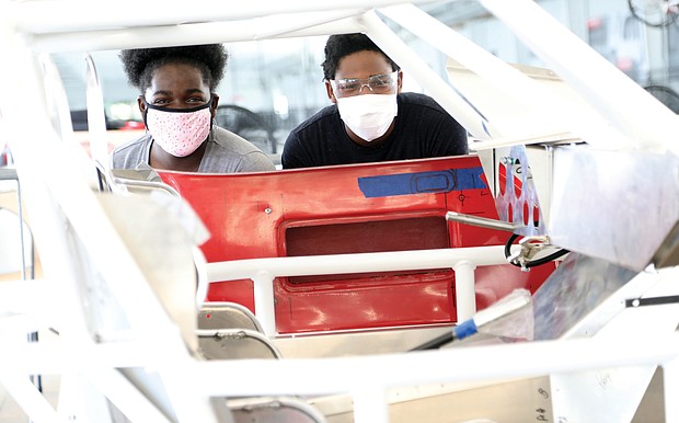 Fraternal twins Aniyah Rawl, left, and her brother, Xavier Rawl, 14, pause for a portrait through the frame of the Dodge Daytona Coupe 500 R that they are helping to build under the tutelage of pioneering aviator Barrington Irving with The Flying Classroom project and Richmond Public Schools. The hands-on work is taking place at Richmond Raceway.