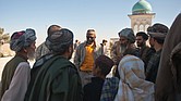 Richard Dickerson, center, meets with local Afghans before a ceremony at Shah Agha Shrine, one of the most holy Islamic sites in the nation, located in the Khakrez District in southern Afghanistan. USAID had worked with U.S. Special Forces and local leaders and villagers to restore the shrine in 2011. Below, Afghan workers at Kandahar Airfield pause to participate in an Eid ceremony at the airfield in 2011.