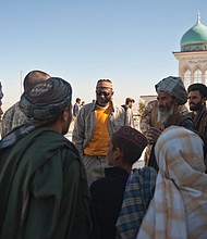 Richard Dickerson, center, meets with local Afghans before a ceremony at Shah Agha Shrine, one of the most holy Islamic sites in the nation, located in the Khakrez District in southern Afghanistan. USAID had worked with U.S. Special Forces and local leaders and villagers to restore the shrine in 2011. Below, Afghan workers at Kandahar Airfield pause to participate in an Eid ceremony at the airfield in 2011.