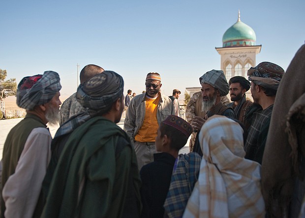 Richard Dickerson, center, meets with local Afghans before a ceremony at Shah Agha Shrine, one of the most holy Islamic sites in the nation, located in the Khakrez District in southern Afghanistan. USAID had worked with U.S. Special Forces and local leaders and villagers to restore the shrine in 2011. Below, Afghan workers at Kandahar Airfield pause to participate in an Eid ceremony at the airfield in 2011.