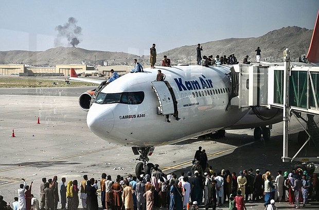 Afghan people climb atop a plane as they wait at the Kabul airport in Kabul
