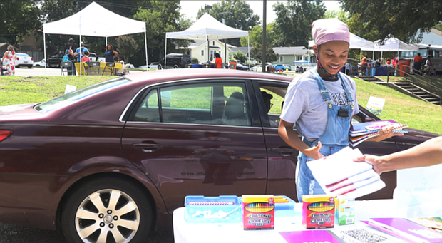 Karma Delvalle, 13, picks up school supplies last Saturday during the 15th Annual “We Care” festival at Overby-Sheppard Elementary School in Highland Park. Because of the pandemic, the festival was set up as a drive-thru event in the school’s driveway, with cars inching along past the booths and people getting out to pick up materials. Festival-goers enjoyed music and picking up the giveaways from various community organizations. COVID-19 testing and vaccines were available at the festival from Capital Area Health Network.