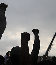 Onlookers raise their fists in the air in solidarity with the removal of the towering statue at Monument and Allen avenues.