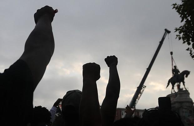 Onlookers raise their fists in the air in solidarity with the removal of the towering statue at Monument and Allen avenues.