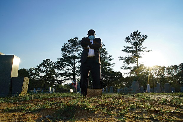 Mortician Shawn Troy stands at the grave of his father, William Penn Troy Sr., at Hillcrest Cemetery outside Mullins, S.C., on Sunday, May 23, 2021. The elder Troy, who developed the cemetery, died of COVID-19 in August 2020, one of many Black funeral directors to succumb to the pandemic. “I don’t think I’ll ever get over it,” he said. “But I’ll get through it.”