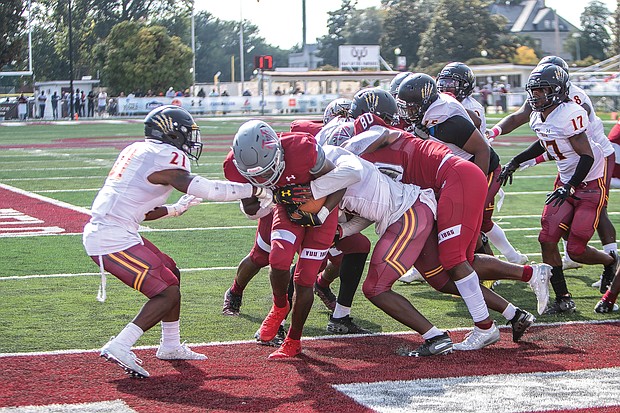 With a gaggle of players clinging to him, Virginia Union University’s Jada Byers pushes his way across the goal line last Saturday for a touchdown. It was the Panthers sole touchdown against Shaw University.
