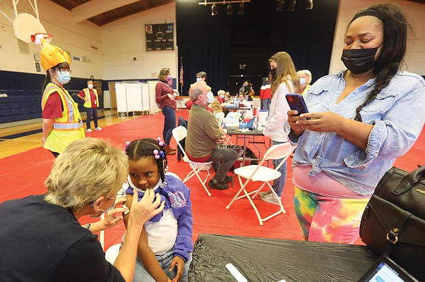 Keisha Spearman, 45, uses her cellphone camera to document her daughter, London, 5, getting her first dose of the COVID-19 vaccine at Fairfield Middle School in Henrico County. Ms. Spearman, her daughter, her mother and grandmother all had the coronavirus last year, canceling Thanksgiving.