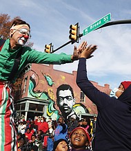 A stilt-walking clown gives a high-five to a child in the crowd.