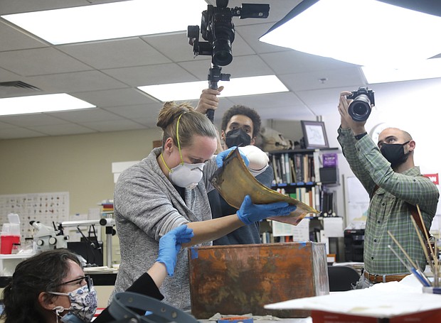 Conservator Gretchen Guidess with the Colonial Williamsburg Foundation, left, assists conservator Sue Donovan of the university of Virginia, in removing items from the copper time capsule found by workers on Monday in the rubble of the Lee statue pedestal on Monument Avenue. The box was opened and unpacked by conservators on Tuesday in the conservation lab at the state Department of Historic Resources.