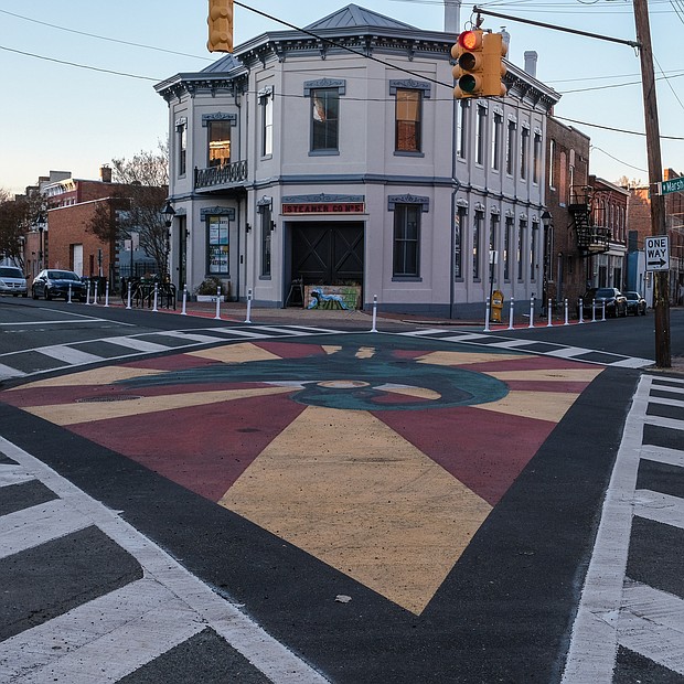 This dramatic and decorative street mural now fills the intersection at Mar- shall Street and Brook Road in Jackson Ward.
The work, painted in the red, black and green colors of the Pan-African flag, stands in front of Gallery 5, an award-winning art space housed in a historic 1849 building that served as the city’s first firehouse and police station.
Venture Richmond and the city’s Public Art Commission teamed with art spaces and businesses to develop the place-making project that was supported in part by a $25,000 grant from Bloomberg Philanthro- pies’ Asphalt Art Initiative. The project, which cost a total of $40,000, produced a new brick plaza and bike rack in front of Gallery 5.
Artist Chris Visions created the mural painted by youth participants at ART 180, a nonprofit center of youth creativity based at 114 W. Marshall St. The central figure is Sankofa, a symbol and word of the Akan people of Ghana meaning “to retrieve.” The symbol is being used as a salute to Jackson Ward’s history as the once proud center of Black business, entertainment and culture.
The mural also is connected to a custom-designed parklet that fills two parking spaces in front of ART 180. The parklet, not pictured here, is one of five the city has sought to install to promote community and businesses.
The initiative came together this year as part of marking the 150th anniversary of the city’s creation of Jackson Ward in 1871. At the time, it was a gerrymandered political district for Black voters. Venture Richmond credited the two art groups, Big Secret, Walter Parks Architects, CB Chandler Construction, Cite Design, Richmond Toolbank and Vanderbilt Properties with helping create the space.