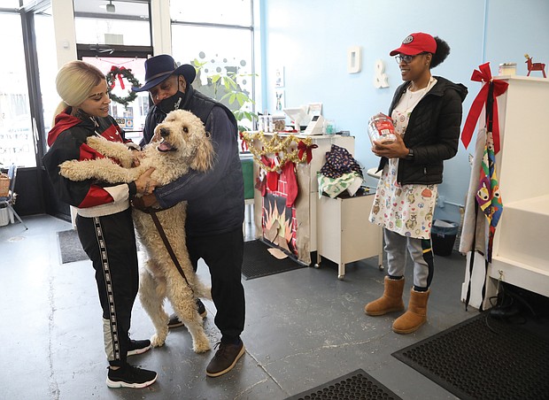 Koda Kong, a year-old Golden Doodle, greets groomer Brittany Smith as he is brought into the dog spa for his holiday bath by his owner, Edward Atkins of Henrico, as Ms. Millett, right, stands by with a dog treat.