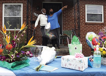 Retired nurse Juliette Stephens Hamilton, left, stands on her front porch in Washington Park as well-wishers offer drive-by greetings to celebrate her 103rd birthday on March 25. Ms. Hamilton welcomed guests and drivers alongside Brenda Dabney Nichols, president of the Washington Park Civic Association, who helped organize the “Parade Drive-By Celebration” with members of Ms. Hamilton’s family.