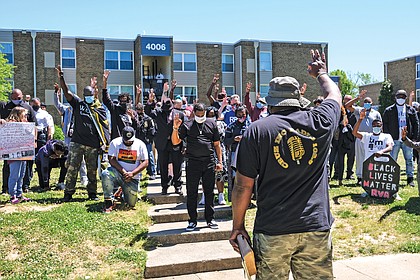Cruz Sherman, founder of Men in Action, leads a prayer outside the apartment complex as those assembled hold up three fingers in honor of the infant who was killed. The stop the violence rally was held May 1.