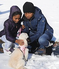 Nicole Lindsay and her 8-year-old daughter, Amira Hill, pause during a snowy walk Tuesday to pet the newest member of the family, Fuzzi, a 2-year-old Bichon Frise. Amira, a fourth-grader engaged in virtual learning at Richmond’s Overby- Sheppard Elementary School, wanted to show Fuzzi around the North Side neighborhood. The family was walking in the 2800 block of Wellington St., where the bright sunshine had melted snow from the sidewalks.