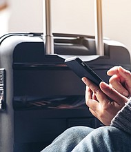 On January 19, Verizon and AT&T turned on their C-band 5G networks which are important set of radio frequencies that will supercharge the internet, and pictured, a woman sitting and using mobile phone with a black baggage for traveling.
Mandatory Credit:	Adobe Stock