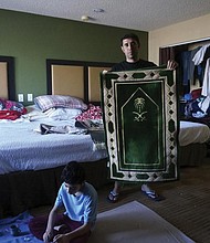 Khial Mohammad Sultani holds the prayer rug that is among his family’s most treasured possessions in the motel room in El Paso, Texas, where they now live. His father brought the rug from Mecca after another son was killed by the Taliban, Mr. Sultani said, and now he brought it to his new life in the United States.