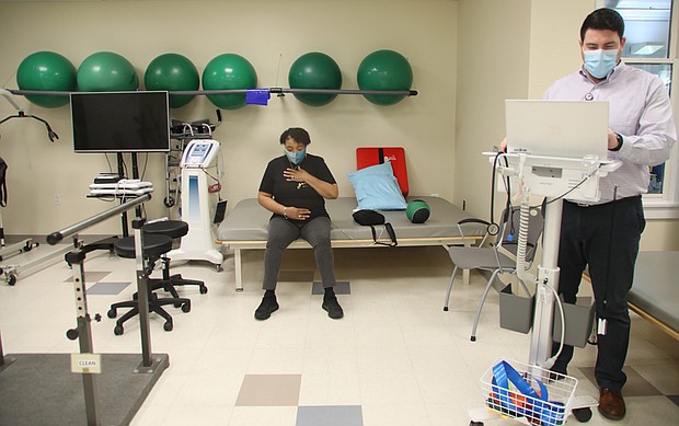 Natarsha Eppes-Kelly sits to catch her breath after completing physical therapy exercises with a weighted four-pound ball. Her therapist, Dr. Jason Seltzer, enters on his computer notes about her progress. Ms. Eppes-Kelly has been undergoing physical therapy at Sheltering Arms Physical Rehabilitation and Therapy Center in Bon Air.