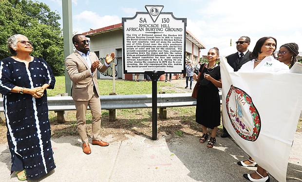 Mayor Levar M. Stoney takes part in unveiling new state history marker for the historic Shockoe Hill Burying Ground, the long forgotten public cemetery for 22,000 Black people at 1305 N. 5th St. at the entry to Highland Park. Joining the mayor at the ceremony Sunday afternoon are Ana F. Edwards of the Sacred Ground Historical Reclamation Project, left, and Lenora C. McQueen, a Texas resident who has led a four-year fight to preserve and protect the burial ground where relatives are buried and who has pushed for the cemetery’s recognition and designation as a national historic site.