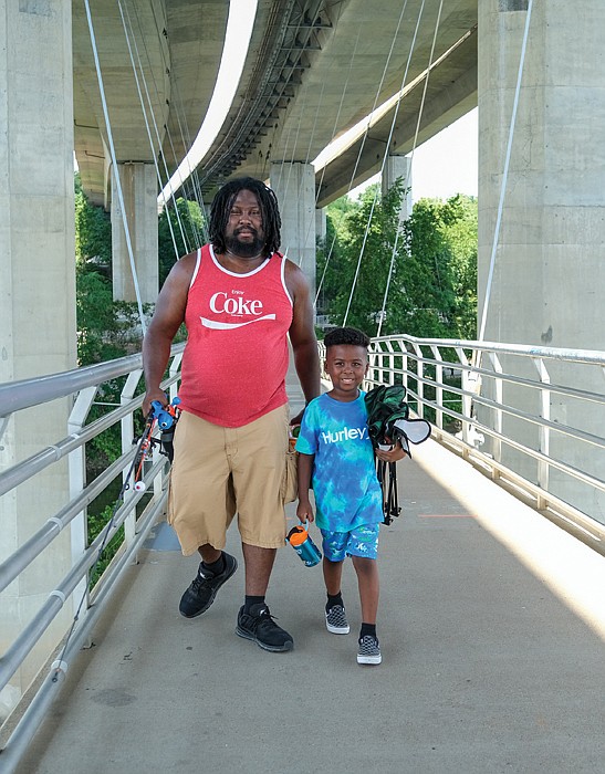 Father and son fishermen, Denzel Terrell and 6-year-old Deion Terrell, trek the pedestrian bridge from Brown’s Island to Belle Isle looking to land a big catch this summer.