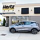 A woman drives a Gray Ghost Metallic 2023 Chevrolet Bolt EUV in front of a Hertz rental location in Michigan. Hertz will begin taking deliveries of the Chevrolet Bolt EV and Bolt EUV in the first quarter of 2023.