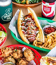 The Brisket Hot Dog is wrapped in bacon with caramelized onions and peppers, pickled jalapeños, mustard, ketchup and mayonnaise. (Photo by Becca Wright)