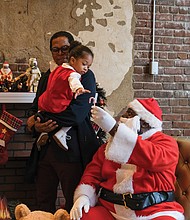 A reluctant Mazir George Harris, 2, needs the support of his grandfather, Dr. Monroe Harris, for his conversation with Soul Santa (Floyd Brown) at the Black History Museum and Cultural Center of Virginia earlier this month.