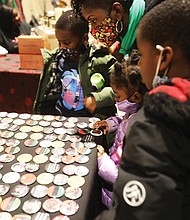 Jennifer Gilliam of Richmond, center, and her children, Marvin III, 7, Leila, 4, and Jameson, 6, admire a display of Afrocentic-themed buttons during the Elegba Folklore Society’s 2022 Capital City Kwanzaa Festival at the Greater Richmond Convention Center Friday, Dec. 30, 2022.