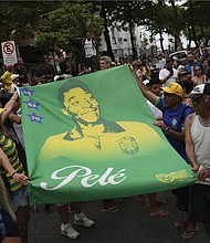 People hold a banner of the late Brazilian soccer great Pelé along the route of his funeral procession from Vila Belmiro stadium to the cemetery in Santos, Brazil, Tuesday, Jan. 3, 2023.