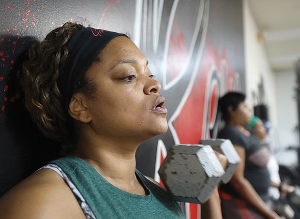 DeAndra Lee, 42, of Henrico County completes a round of strenuous curls while doing a wall squat at Raw Affects Gym on last Saturday.