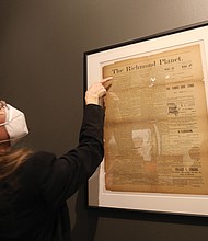 Mari Julienne, a Library of Virginia historian, peers closely at a May 31, 1890, edition of The Richmond Planet, a Black newspaper founded by John Mitchell Jr. This edition details the unveiling of the Robert E. Lee statue.