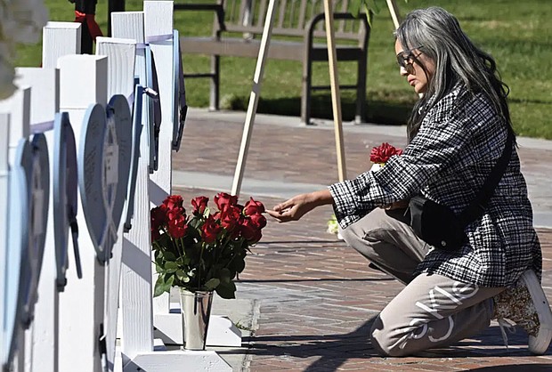 Lisa Lozano touches roses in front of wooden hearts with messages on them at a makeshift memorial Tuesday in front of the Monterey Park City Hall in Monterey Park, Calif. A gunman killed multiple people at the Star Ballroom Dance Studio late Saturday, Jan. 21, amid Lunar New Year celebrations in the predominantly Asian-American community of Monterey Park.