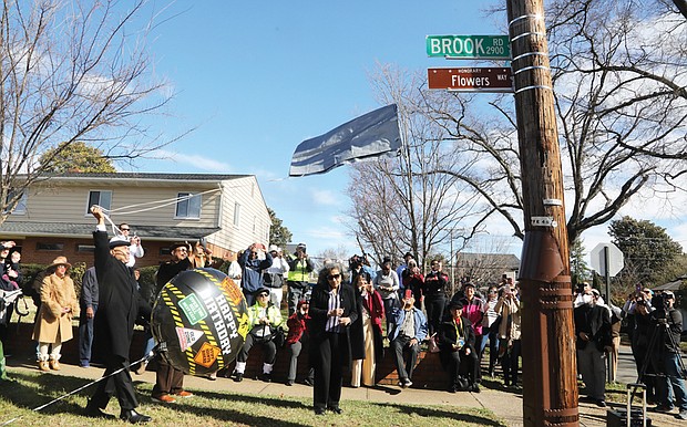 At the corner of Hammond and Brook Road in Richmond’s Edgehill neighborhood, Gary Flowers, left, pulls the signage cover strings Monday, as his sister, Jan Flowers, stands with him. Along with other family, friends and neighbors, the son and daughter of Stafford Alvin Flowers and Ella Lee Fountain Flowers unveil the honorary street sign, Flowers Way, that honors their father and mother.
Stafford Alvin Flowers, who died in 2011, was a brick mason and owner of a contracting business. He also was a co-founder of the Metropolitan Business League, and a regional director for the National Business League, which evolved from the Negro Business League founded by Booker T. Washington in 1900. Ella Lee Fountain Flowers, a former Virginia Union University and Richmond Public Schools educator, died May 15, 2022. Mrs. Flowers was an 80-year member of Delta Sigma Theta Sorority and a lifelong member of the NAACP, serving as the secretary for the Richmond Chapter.
The street dedication was initiated by 3rd District North Side City Council woman Ann-Frances Lambert, who wants the history of Black Northside Richmond locked in for all to know. She reminded people that a large percentage of Black Americans, when researching their genealogy, realize they have a connection to Richmond.