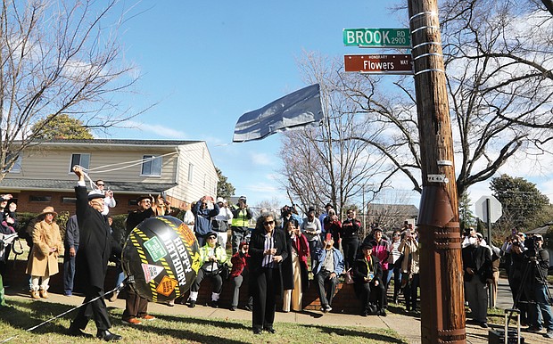 At the corner of Hammond and Brook Road in Richmond’s Edgehill neighborhood, Gary Flowers, left, pulls the signage cover strings Monday, as his sister, Jan Flowers, stands with him. Along with other family, friends and neighbors, the son and daughter of Stafford Alvin Flowers and Ella Lee Fountain Flowers unveil the honorary street sign, Flowers Way, that honors their father and mother.
Stafford Alvin Flowers, who died in 2011, was a brick mason and owner of a contracting business. He also was a co-founder of the Metropolitan Business League, and a regional director for the National Business League, which evolved from the Negro Business League founded by Booker T. Washington in 1900. Ella Lee Fountain Flowers, a former Virginia Union University and Richmond Public Schools educator, died May 15, 2022. Mrs. Flowers was an 80-year member of Delta Sigma Theta Sorority and a lifelong member of the NAACP, serving as the secretary for the Richmond Chapter.
The street dedication was initiated by 3rd District North Side City Council woman Ann-Frances Lambert, who wants the history of Black Northside Richmond locked in for all to know. She reminded people that a large percentage of Black Americans, when researching their genealogy, realize they have a connection to Richmond.