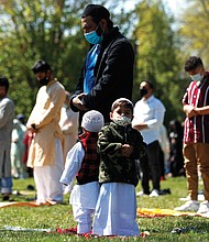 Two children stand with their father as he and other Muslims perform an Eid al-Fitr prayer in May 2021 in an outdoor open area, marking the end of the fasting month of Ramadan in Morton Grove, Ill.