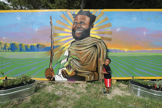 “That’s my daddy,” said 5-year-old Anais Lewis of Roanoke, while staring at the mural of his father, John R. Lewis, whose image and life was memorialized on May 26 at the Sankofa Community Orchard, 301 Covington Road on Richmond’s South Side. Mr. Lewis, who died in January 2021, taught students how to grow their own food and spent time “hanging out” in the garden, often keeping youngsters out of harm’s way as they got their hands dirty together. Mr. Lewis was the co-founder and executive director of Renew Richmond, a nonprofit that operated several urban agricultural sites and sometimes had pop-up stands where fresh produce that was grown and harvested by local Black youthS and adults was also often sold by them too. He advocated for Black communities to understand the power of gardening and self-sufficiency.
Duron Chavis, the founder of the Sankofa Community Garden, said Mr. Lewis was one of the “founding fathers of Black urban agriculture in the City of Richmond.” The mural was created by lead painter Sir James L. Thornhill assisted by R. Vashti Woods, both of Richmond.