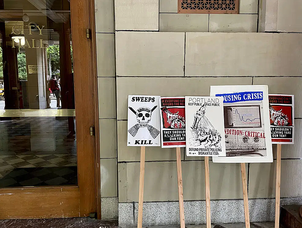 Protest signs condemning a measure in Portland City Council that would ban homeless camps during the daytime in most public places are lined up next to one of the doors of City Hall in Portland, Ore. on Wednesday, May 31, 2023 (AP Photo/Claire Rush)