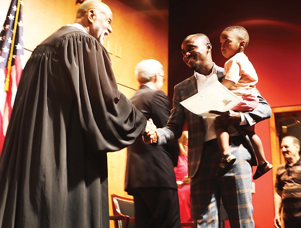 Newly sworn-in American citizen Eric Ackaah, who is from Ghana, carries his 21-month-old son Noah Ackaah across the stage at the Virginia Museum of History & Culture on Tuesday.