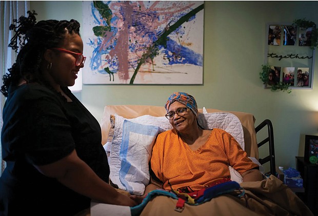 Constance Guthrie, who is 74, sits in a hospital-style bed propped up by a pillow. Her daughter, Jessica Guthrie, stands next to the bed, smiling. She was diagnosed with Alzheimer’s disease at age 66. About 14% of Black people in America over the age of 65 have Alzheimer’s, compared with 10% of white people, according to the Centers for Disease Control and Prevention. The disparity is likely even more, because many Black people aren’t correctly diagnosed.