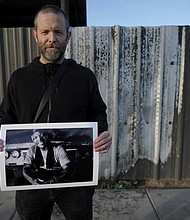 Documentary photographer Eric Elmore displays one of his images of Roosevelt White III in Phoenix at the site of a fire where Mr. White lived in a tent before he died last September.