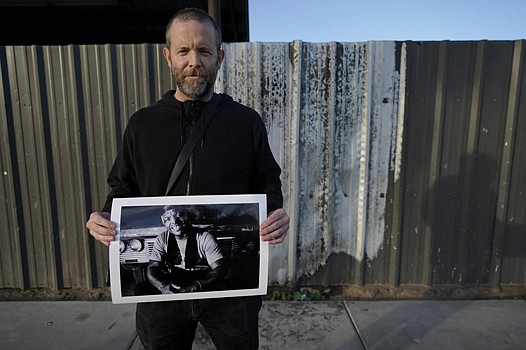 Documentary photographer Eric Elmore displays one of his images of Roosevelt White III in Phoenix at the site of a fire where Mr. White lived in a tent before he died last September.