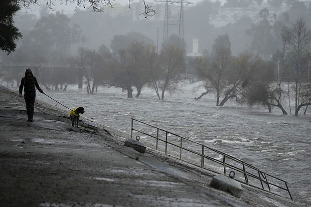 A man walks his dog on the edge of the Los Angeles River, carrying stormwater downstream on February 4 in Los Angeles. The second of back-to-back atmospheric rivers battered California, flooding roadways and knocking out power to hundreds of thousands.
Mandatory Credit:	Damian Dovarganes/AP
