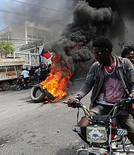 People drive past a burning blockade as demonstrators hold a protest calling for the resignation of Haitian Prime Minister Ariel Henry outside the Canadian Embassy, in Port-au-Prince, Haiti, February 25.
Mandatory Credit:	Ralph Tedy Erol/Reuters via CNN Newsource